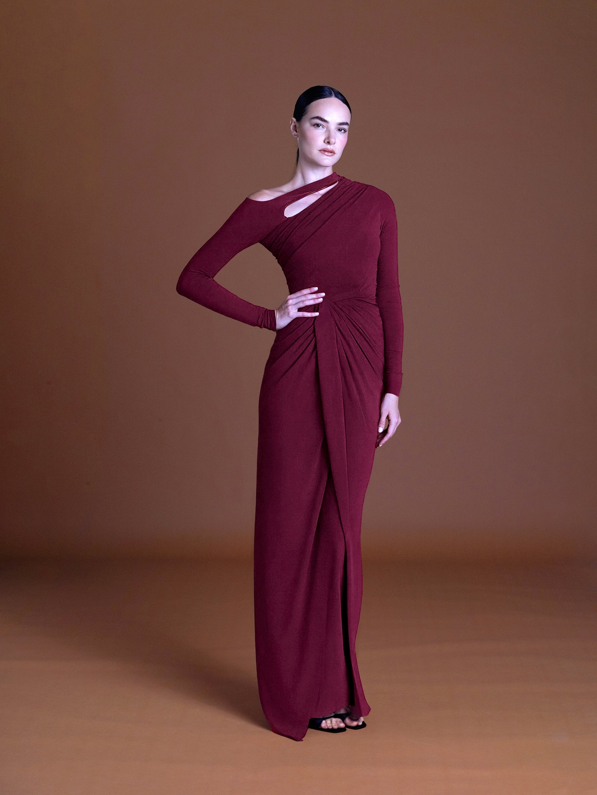 Woman wearing elegant pink cape dress with draped detail against brown background