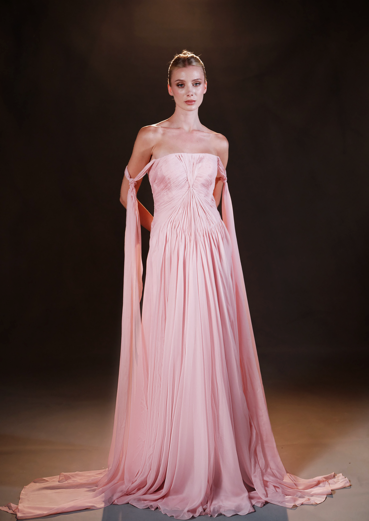 Elegant woman in a burgundy velvet long-sleeve midi dress with floral waist detail on a pink gradient background.