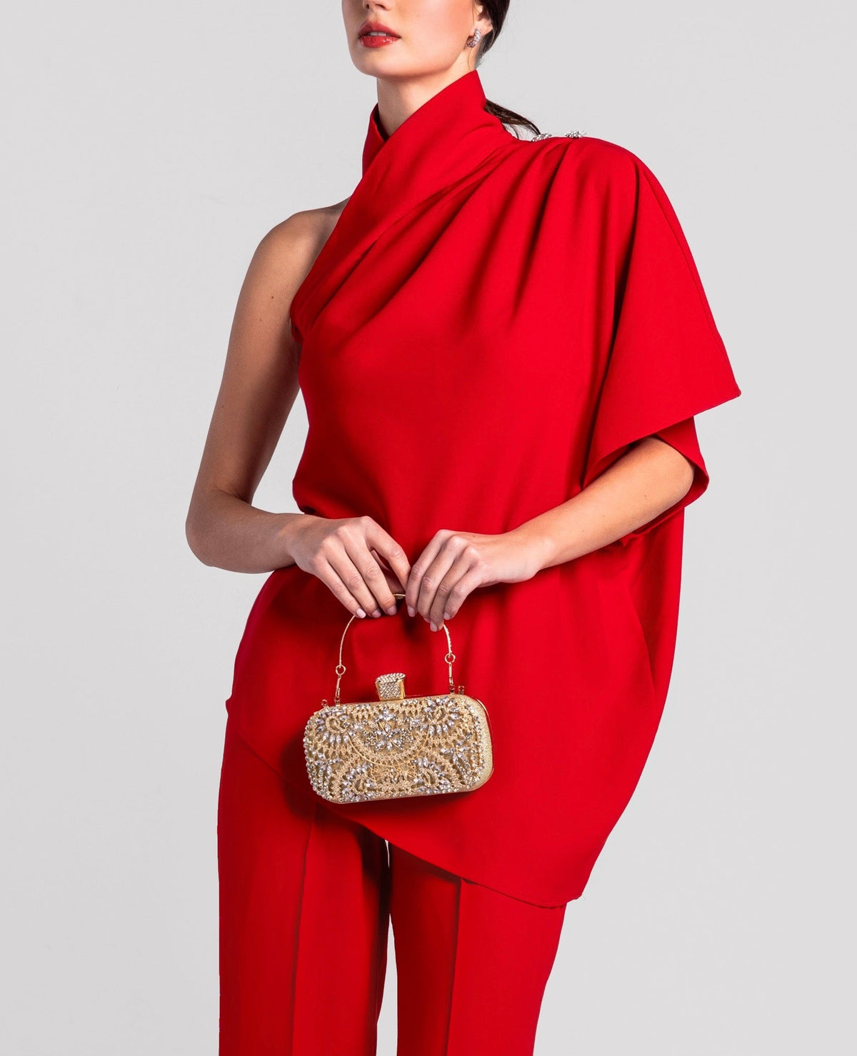Woman in elegant red one-shoulder jumpsuit holding a gold embellished clutch